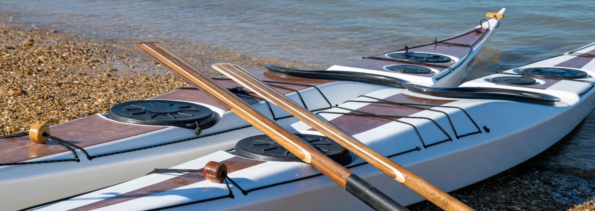 Dos kayaks de mar de madera Nautilus y palas groenlandesas en la orilla