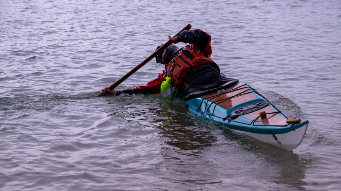 Palista practicando técnica con pala groenlandesa en un kayak de mar de madera